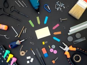 Miscellaneous office tools including sticky notes, a screwdriver, erasers, and paperclips arranged on a dark gray surface.