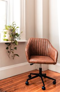 A brown leather swivel chair on a wood floor next to a windowsill with a potted vine.